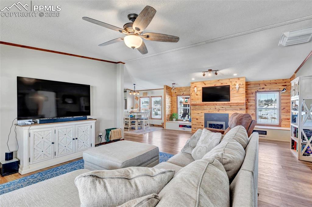 Living area featuring wood finished floors, a textured ceiling, crown molding, a large fireplace, and ceiling fan