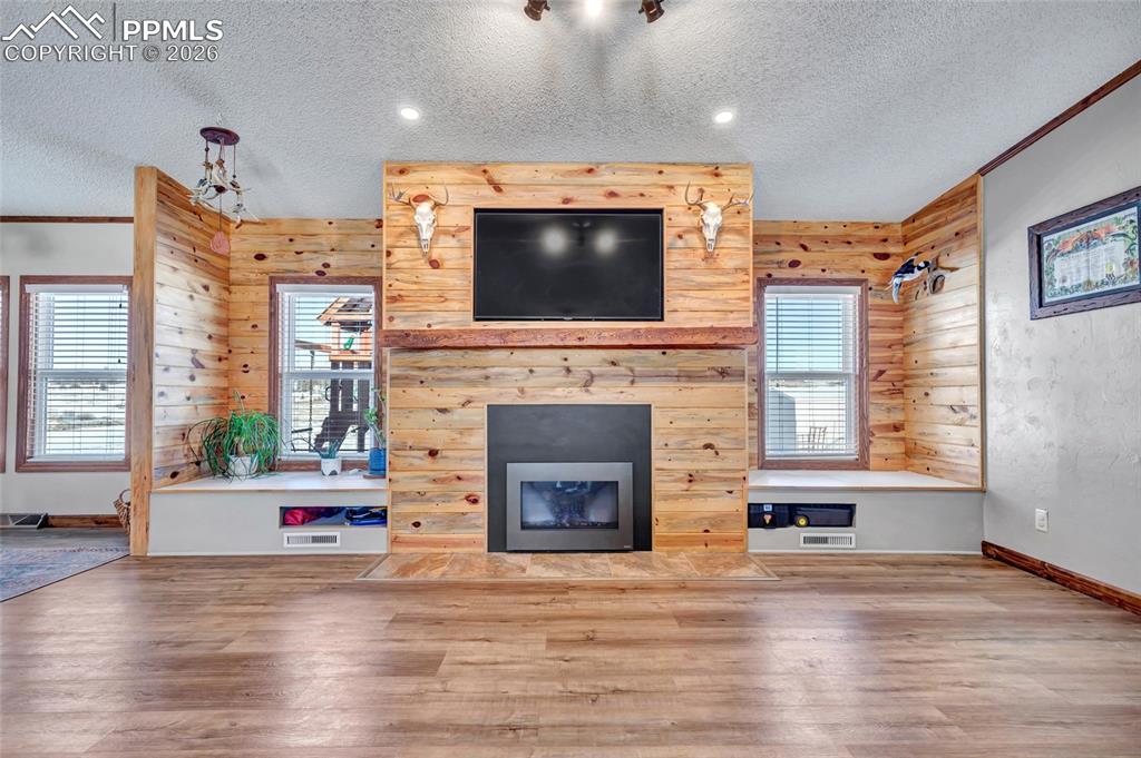 Unfurnished living room with a fireplace with flush hearth, a textured ceiling, wood finished floors, and wooden walls
