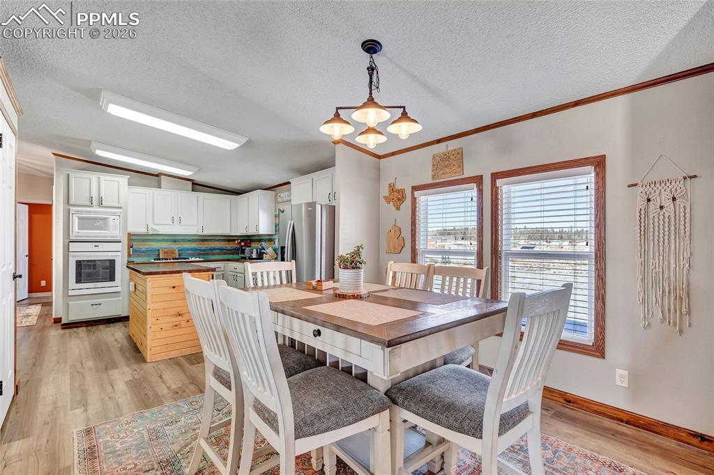 Dining space featuring crown molding, vaulted ceiling, light wood-style flooring, a textured ceiling, and a chandelier