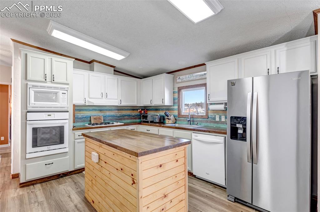 Kitchen featuring white appliances, vaulted ceiling, a textured ceiling, white cabinets, and decorative backsplash