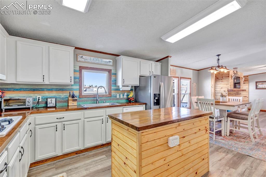 Kitchen with butcher block counters, a kitchen island, crown molding, a textured ceiling, and white cabinets