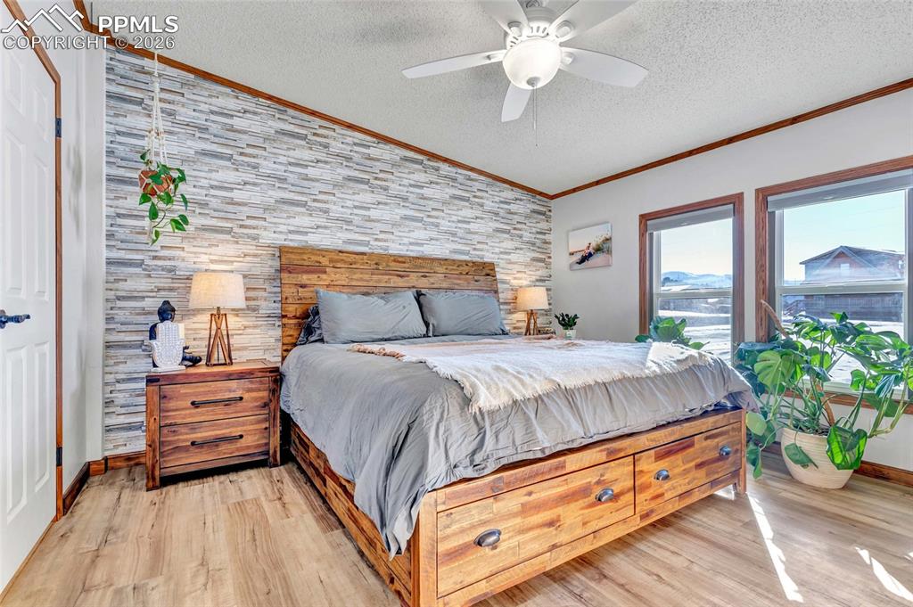 Bedroom with light wood-style flooring, a textured ceiling, ceiling fan, ornamental molding, and an accent wall