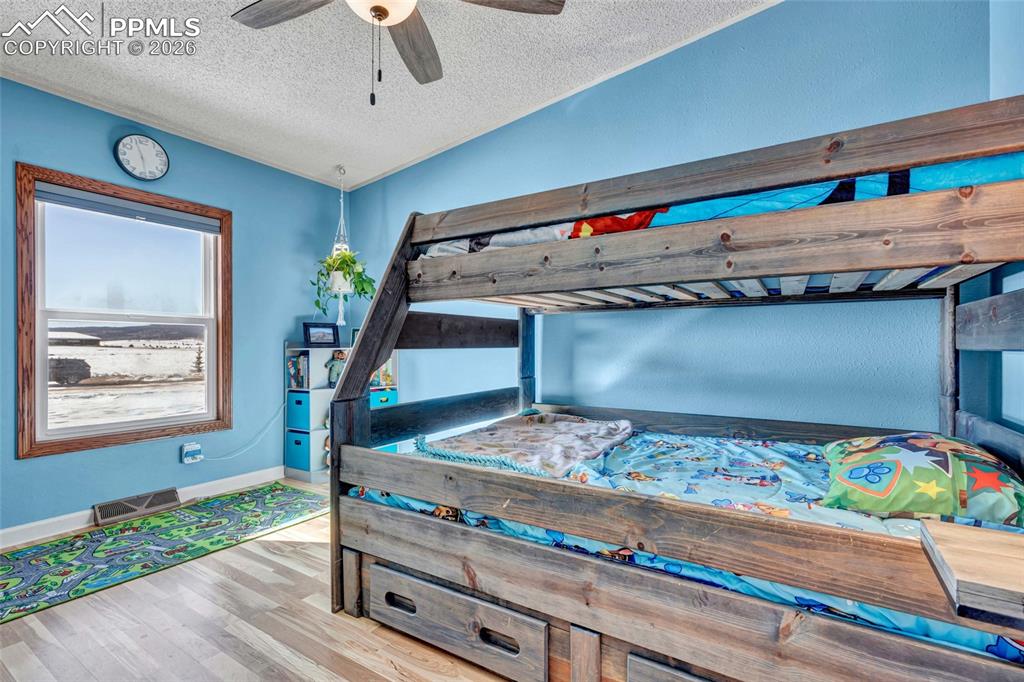 Bedroom with a textured ceiling, light wood-style floors, a ceiling fan, and vaulted ceiling