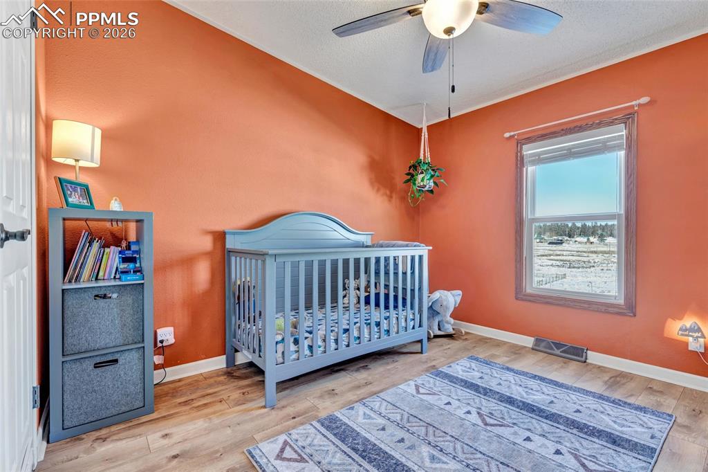Bedroom featuring a crib, light wood-style floors, and ceiling fan