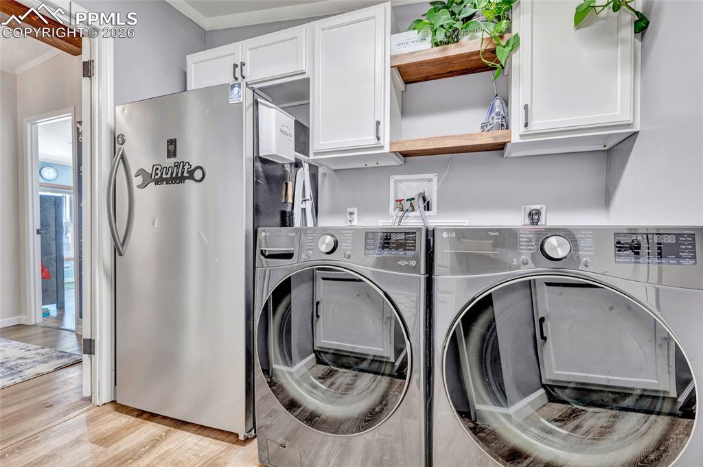 Washroom featuring light wood finished floors, independent washer and dryer, crown molding, and cabinet space