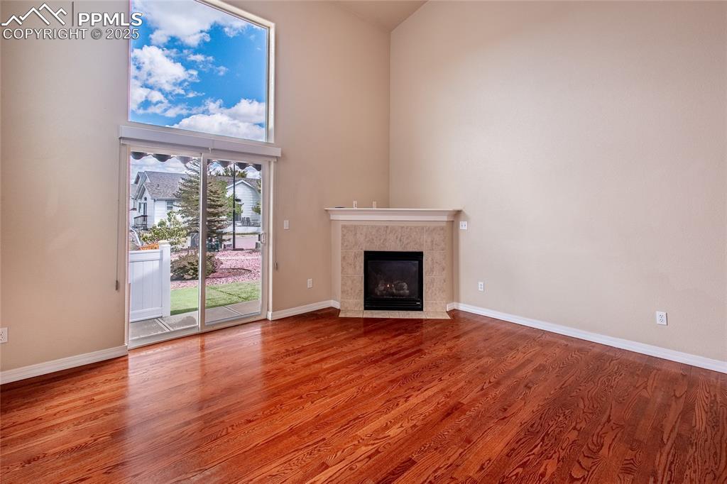 Unfurnished living room with light wood-style flooring, a tile fireplace, and a high ceiling