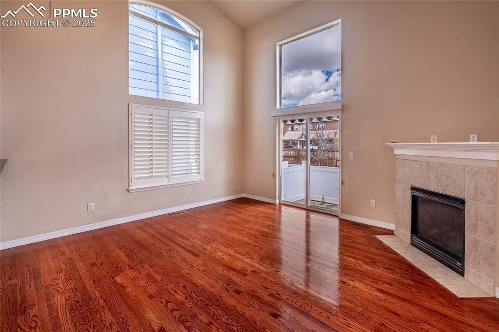 Unfurnished living room featuring a high ceiling, a tiled fireplace, and wood finished floors
