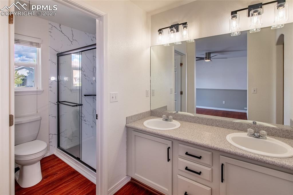 Full bath with dark wood-type flooring, a marble finish shower, double vanity, and a ceiling fan
