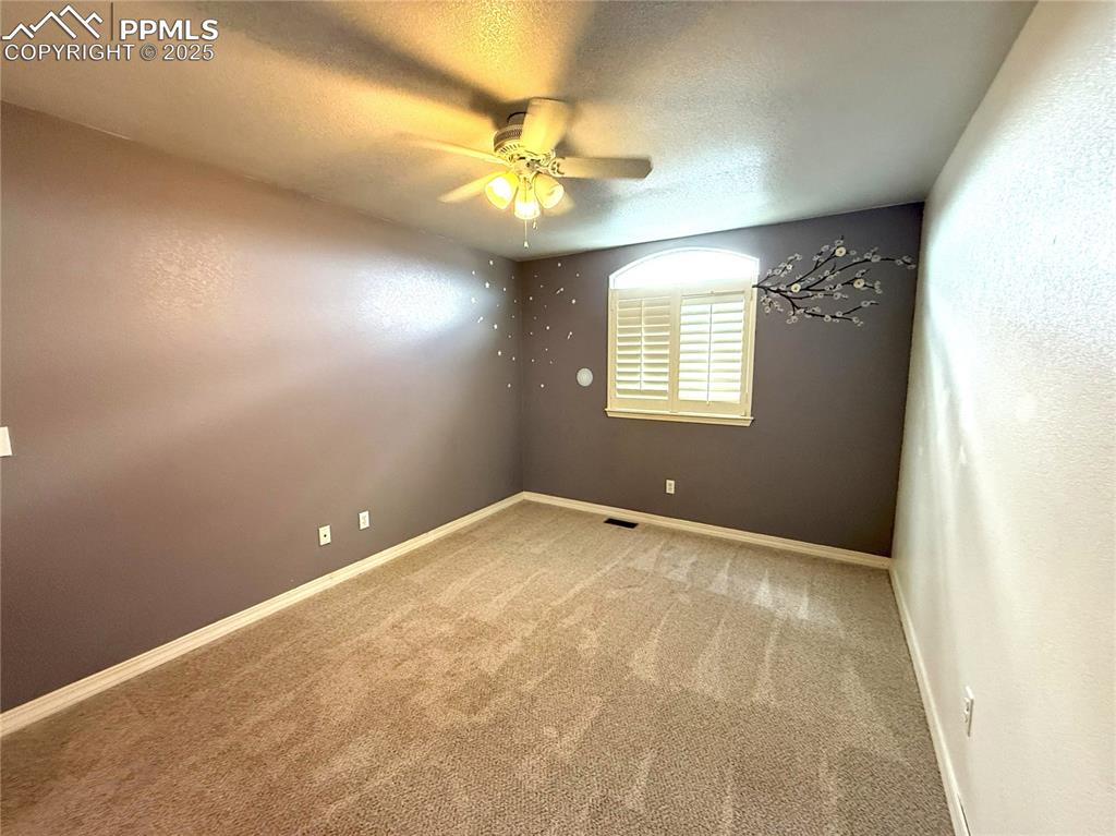 Carpeted empty room with a textured ceiling, ceiling fan, and a textured wall