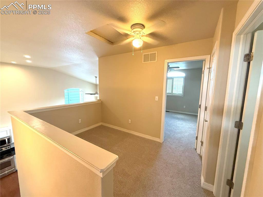Hallway featuring a textured ceiling, carpet flooring, an upstairs landing, vaulted ceiling, and attic access