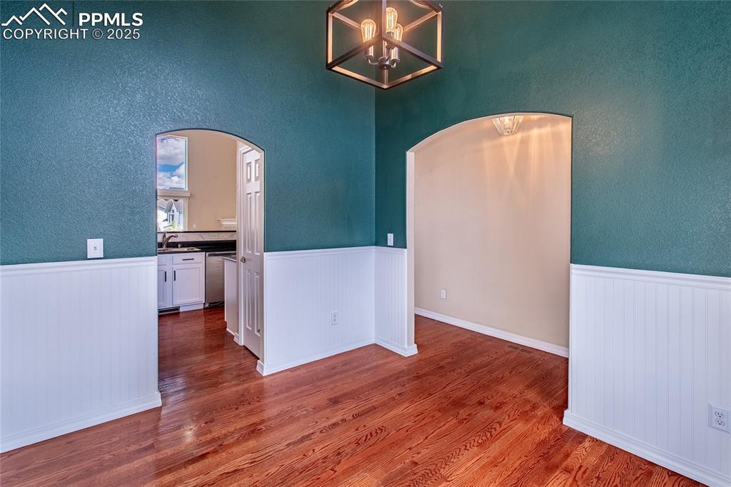 Unfurnished dining area featuring dark wood finished floors, a textured wall, a chandelier, and arched walkways