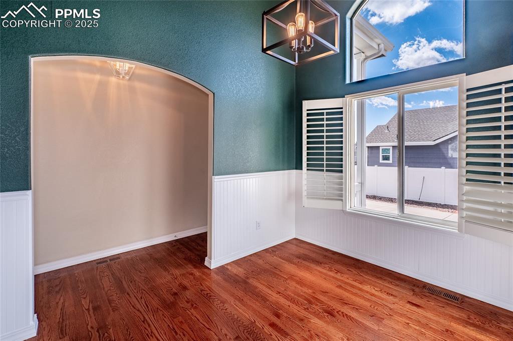Unfurnished dining area with wood finished floors, a chandelier, wainscoting, and arched walkways
