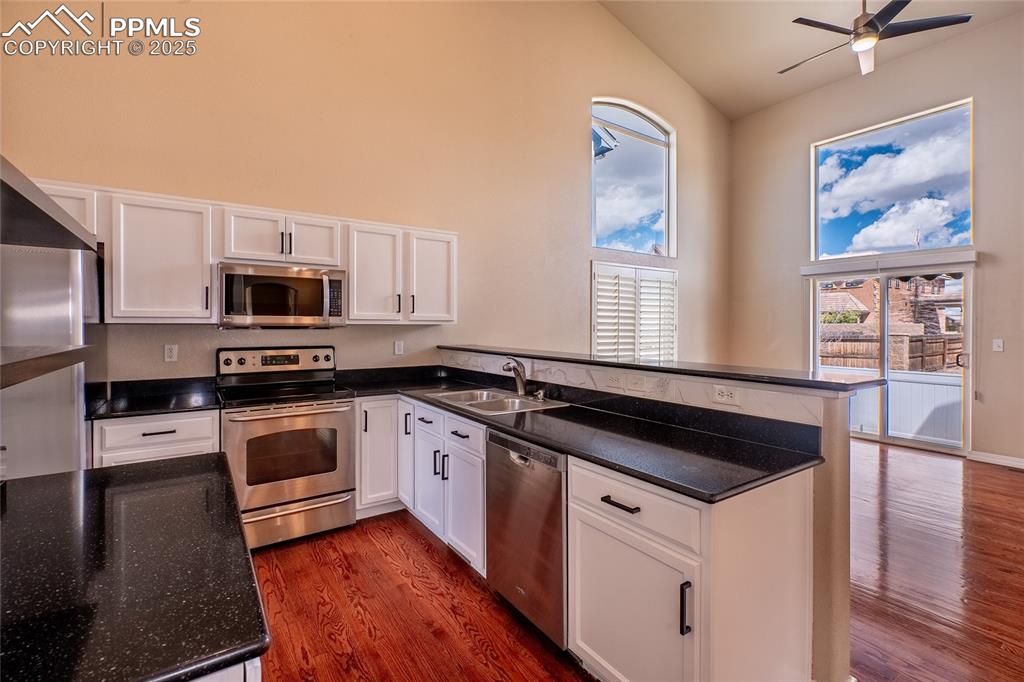 Kitchen with white cabinetry, stainless steel appliances, a peninsula, healthy amount of natural light, and a towering ceiling