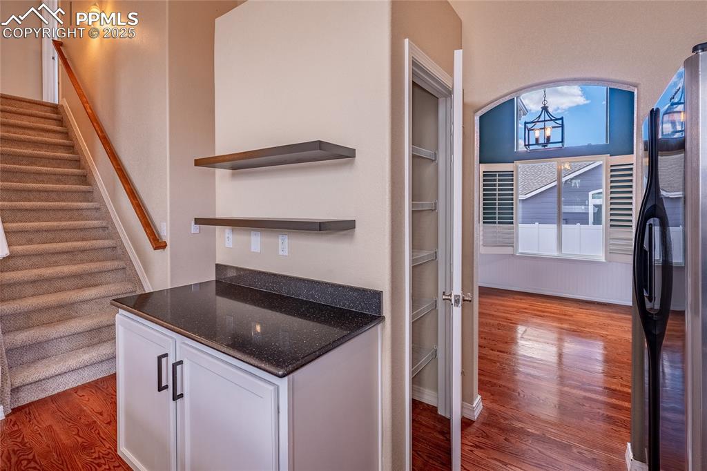 Kitchen with dark wood-style flooring, white cabinetry, open shelves, freestanding refrigerator, and dark stone counters