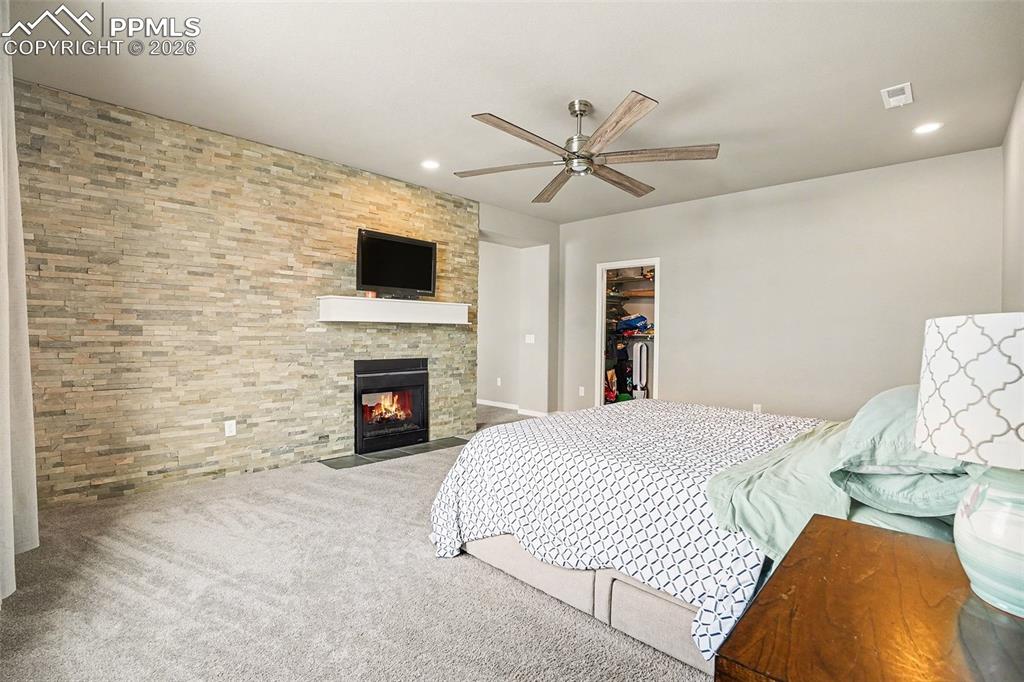 Carpeted bedroom featuring a fireplace, ceiling fan, a walk in closet, and recessed lighting