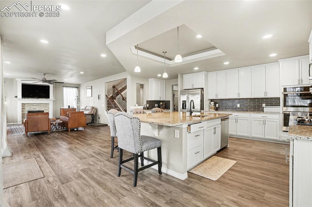 Kitchen featuring white cabinets, a tray ceiling, a breakfast bar, light stone countertops, and hanging light fixtures