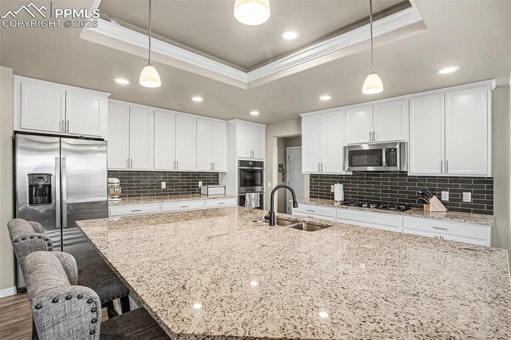 Kitchen with ornamental molding, white cabinetry, appliances with stainless steel finishes, a kitchen breakfast bar, and a raised ceiling