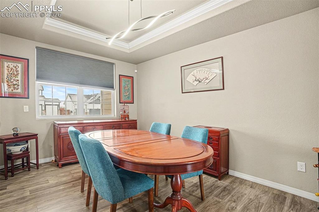 Dining space with light wood-style flooring, ornamental molding, and a tray ceiling