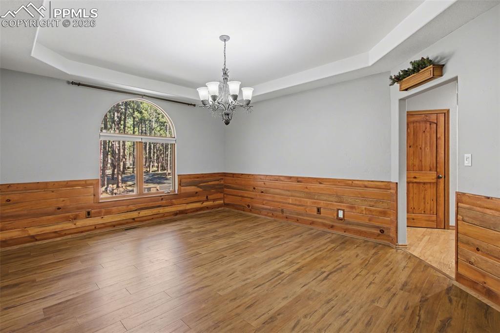Spare room featuring a tray ceiling, wainscoting, a chandelier, wooden walls, and wood-type flooring