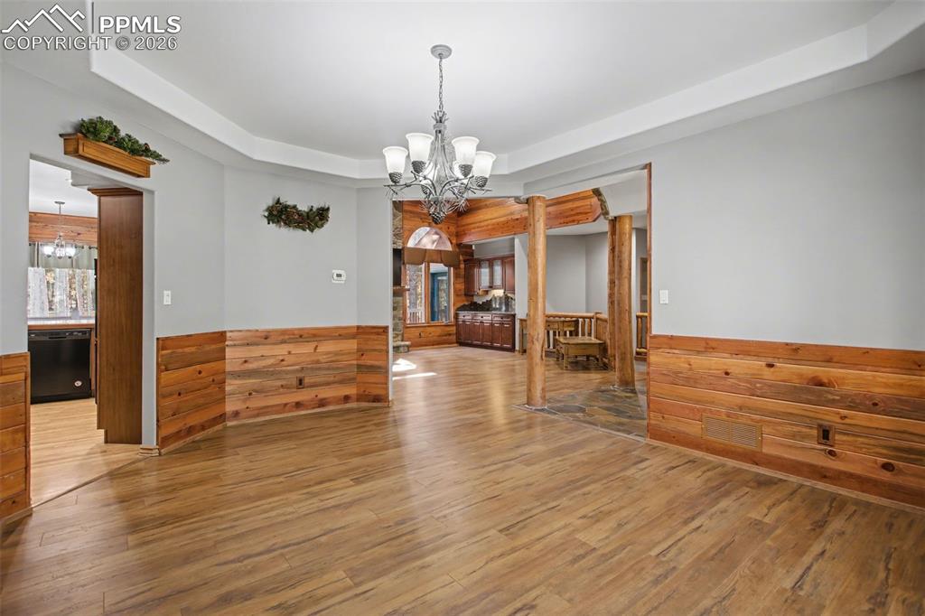 Unfurnished dining area with hanging lights, a raised ceiling, wood walls, a wainscoted wall, and hardwood / wood-style floors