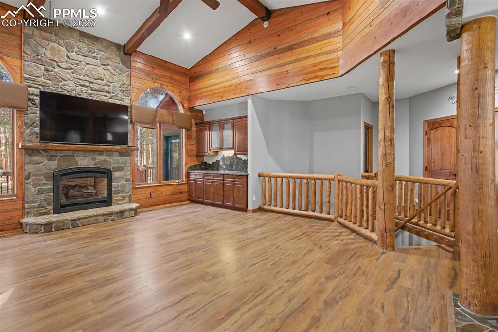 Unfurnished living room featuring light wood-style floors, wood walls, lofted ceiling, and a stone fireplace