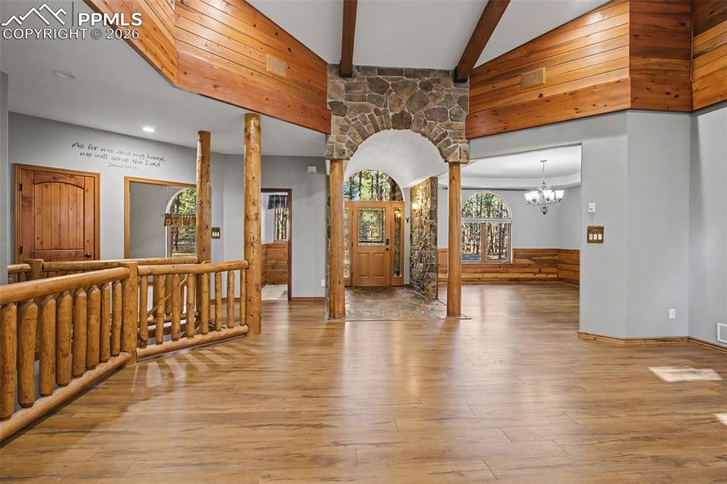 Entrance foyer featuring ornate columns, light wood-style floors, suspended lighting, arched walkways, and healthy amount of natural light