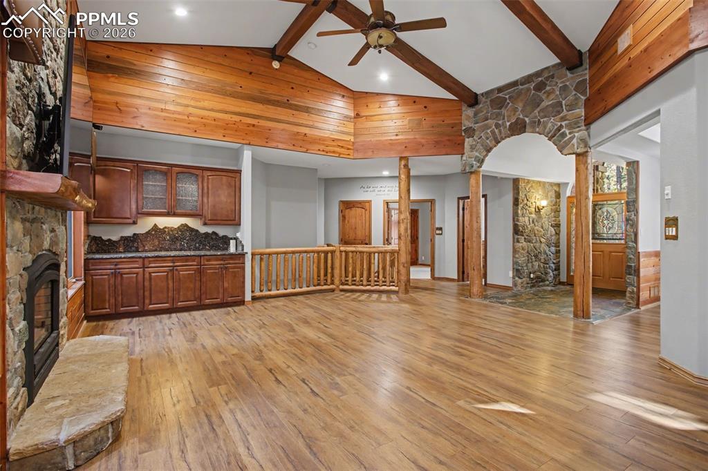 Unfurnished living room with a stone fireplace, light wood-style flooring, ceiling fan, and decorative columns