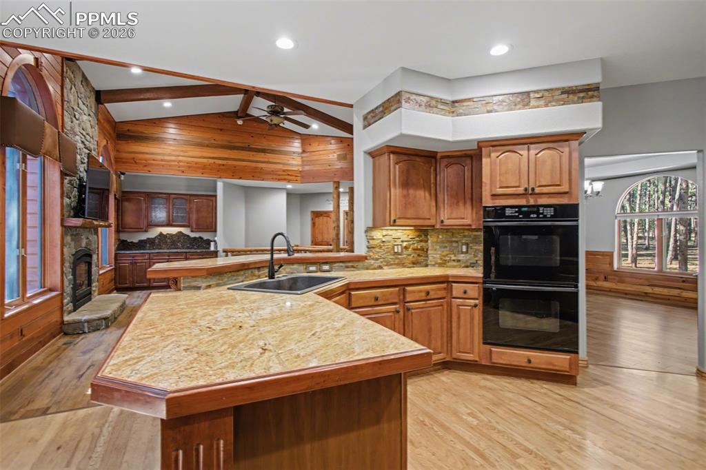 Kitchen with a peninsula, wood finish cabinetry, lofted ceiling, light wood finished floors, and a fireplace