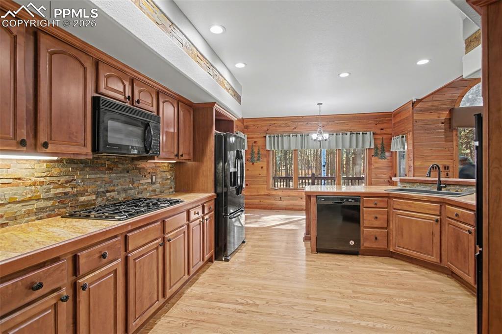 Kitchen with light countertops, black appliances, light wood-style flooring, wood finish cabinetry, and wood walls