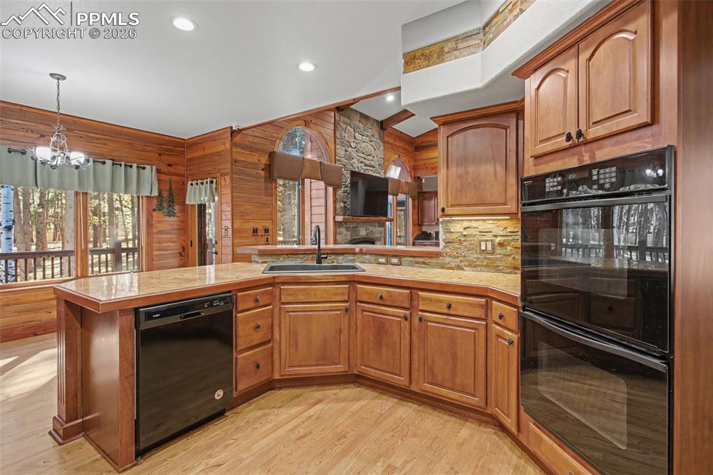 Kitchen featuring black appliances, a peninsula, light countertops, wood finish cabinetry, and wooden walls