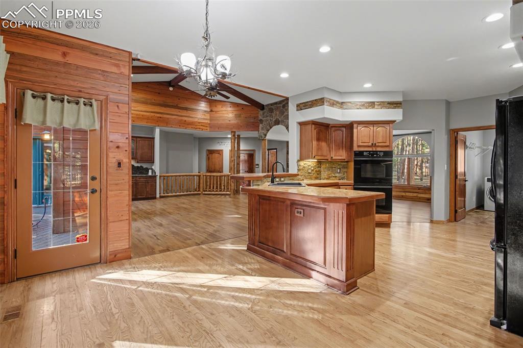 Kitchen featuring light wood-type flooring, a chandelier, black appliances, wood finish cabinetry, and open floor plan