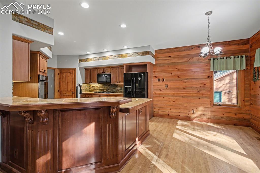 Kitchen with light wood finished floors, wood finish cabinetry, black appliances, a peninsula, and a kitchen bar