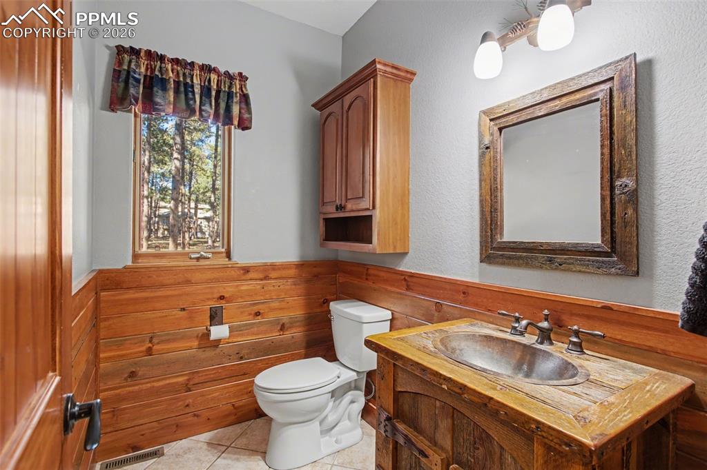 Bathroom featuring vanity, a wainscoted wall, wooden walls, and light tile patterned flooring