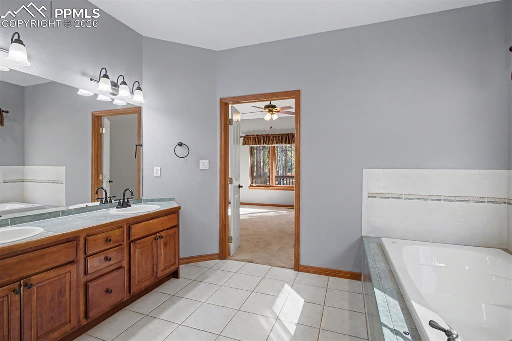 Bathroom featuring a bath, double vanity, light tile patterned flooring, and ceiling fan