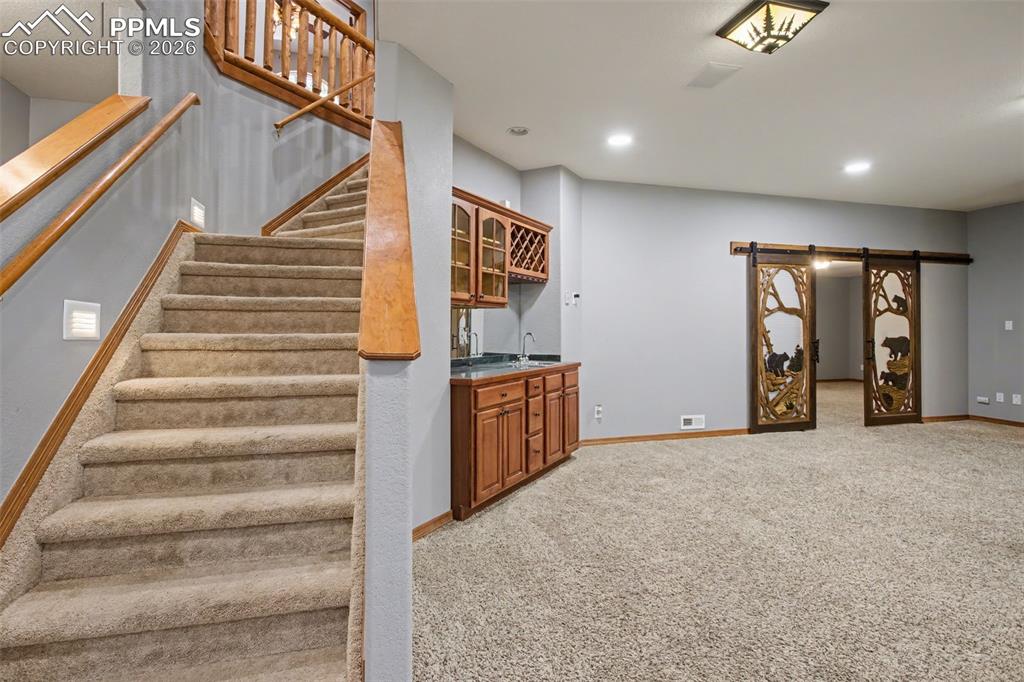Stairs featuring carpet, wet bar, a barn door, and recessed lighting