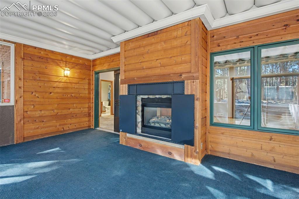 Unfurnished living room with wooden walls, carpet, and a stone fireplace