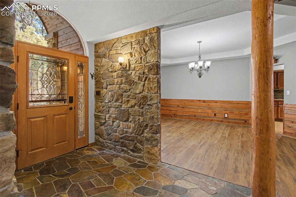 Entrance foyer with wooden walls, stone flooring, wainscoting, and a chandelier