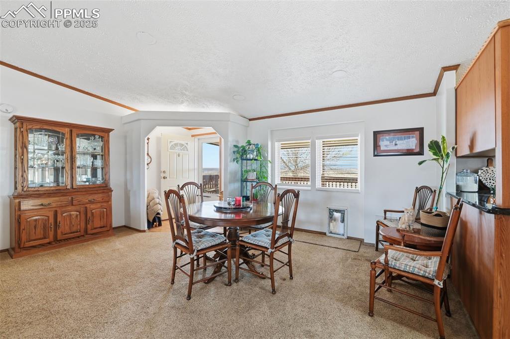Dining area with arched walkways, ornamental molding, a textured ceiling, and light colored carpet