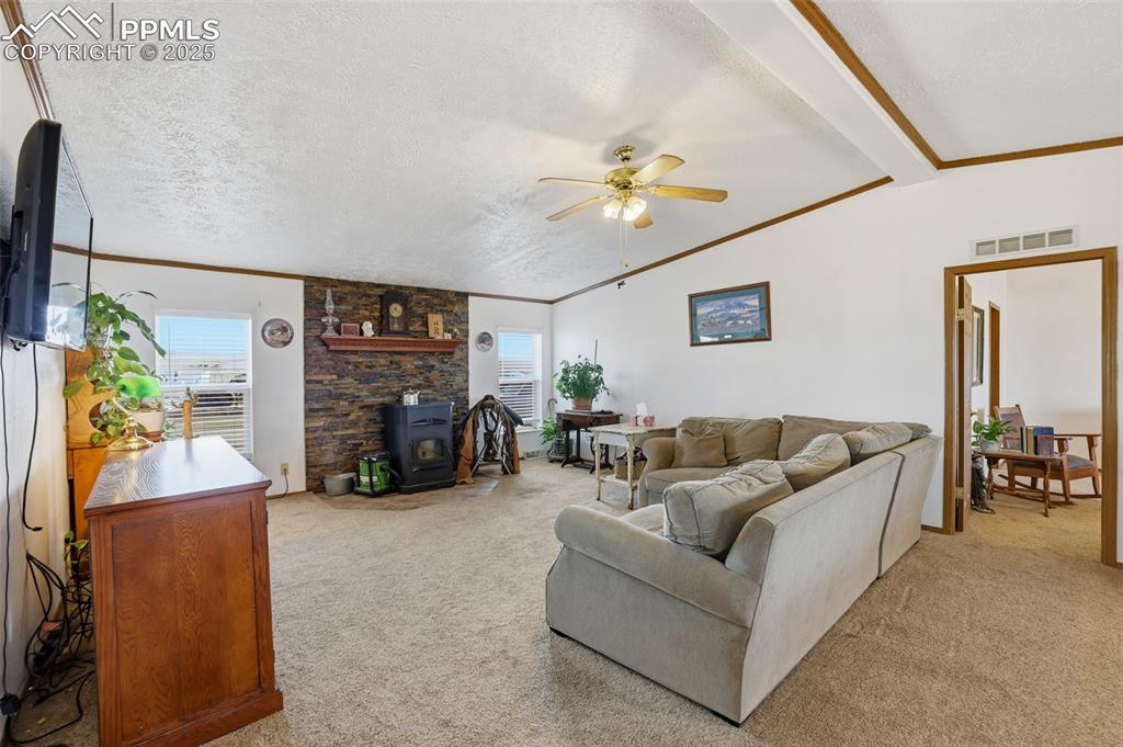 Living room with a wood stove, a textured ceiling, ornamental molding, light carpet, and lofted ceiling