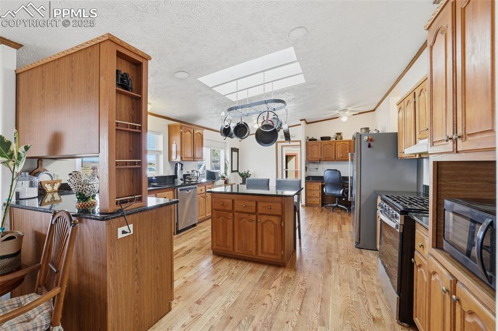Kitchen with crown molding, open shelves, brown cabinets, stainless steel appliances, and a center island