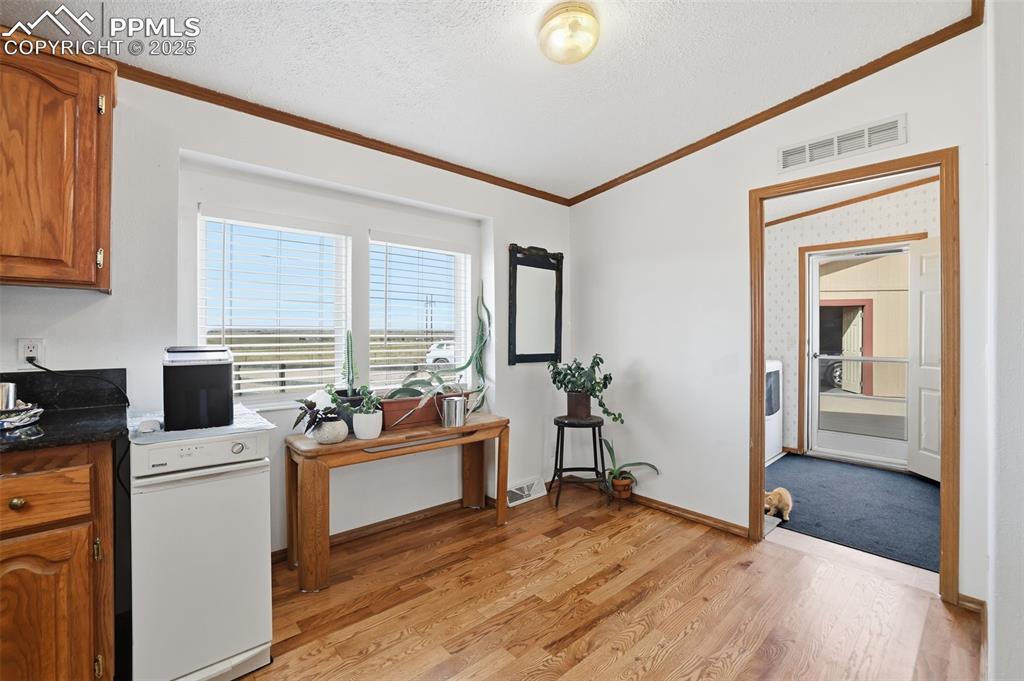 Kitchen featuring brown cabinetry, a textured ceiling, vaulted ceiling, dark countertops, and ornamental molding