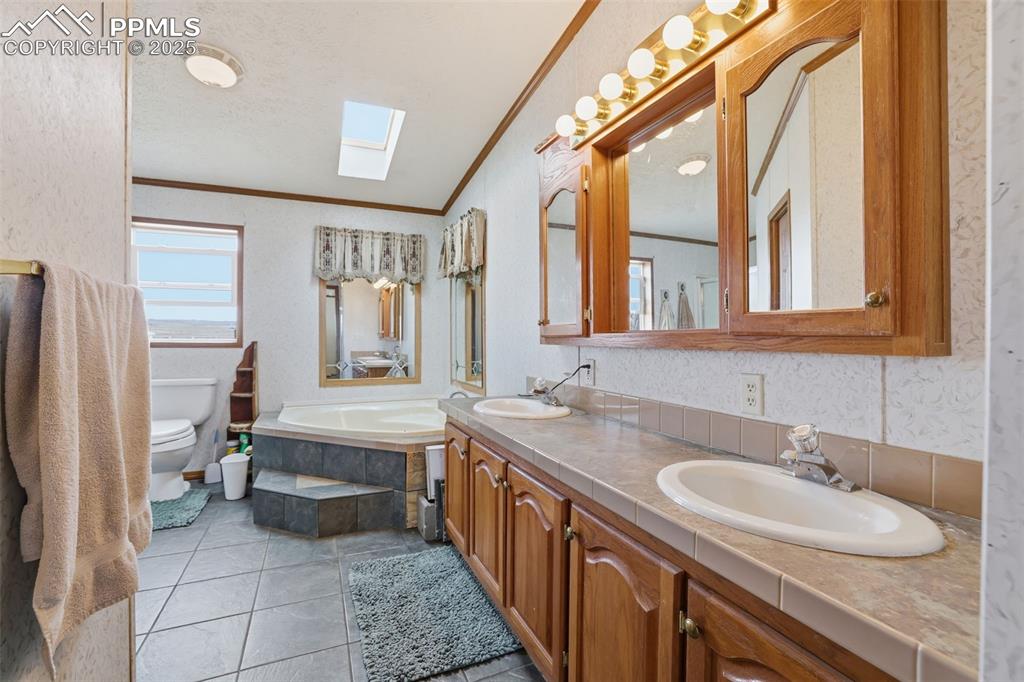 Full bath featuring a skylight, a bath, double vanity, ornamental molding, and a textured ceiling