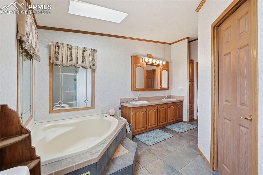 Full bathroom with ornamental molding, a bath, double vanity, a skylight, and light tile patterned floors