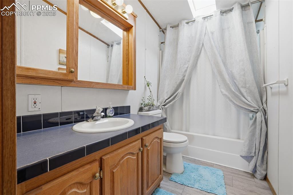 Bathroom featuring shower / bathtub combination with curtain, vanity, and wood finish floors