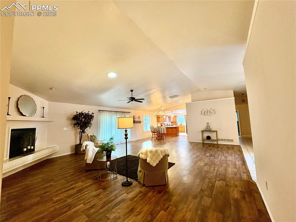 Living area with a fireplace with raised hearth, dark wood-type flooring, lofted ceiling, a ceiling fan, and a chandelier