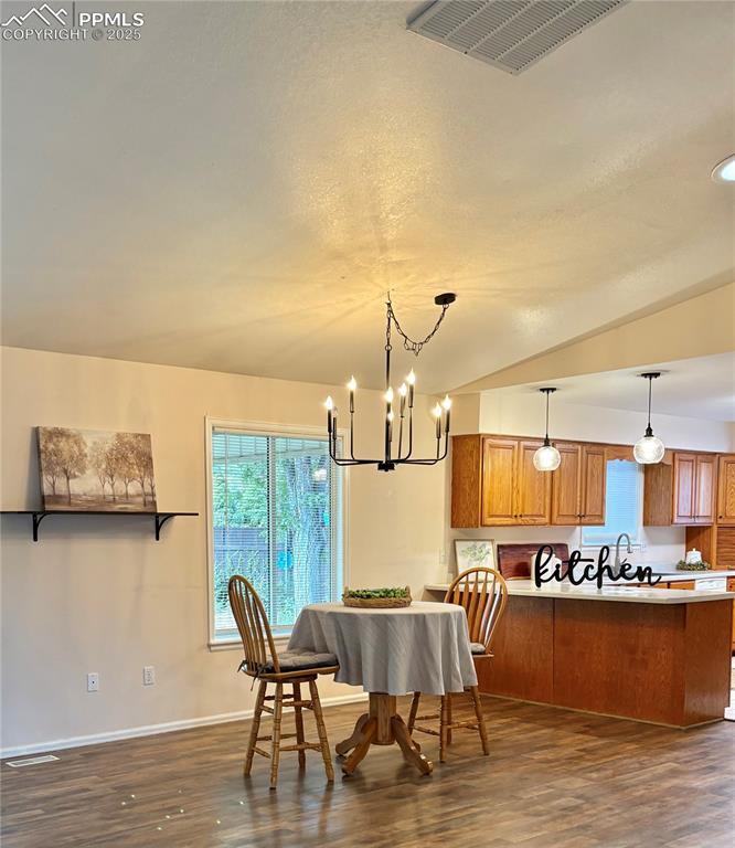 Dining area featuring dark wood-type flooring, a chandelier, and vaulted ceiling