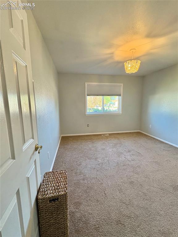 Carpeted empty room featuring baseboards and a chandelier