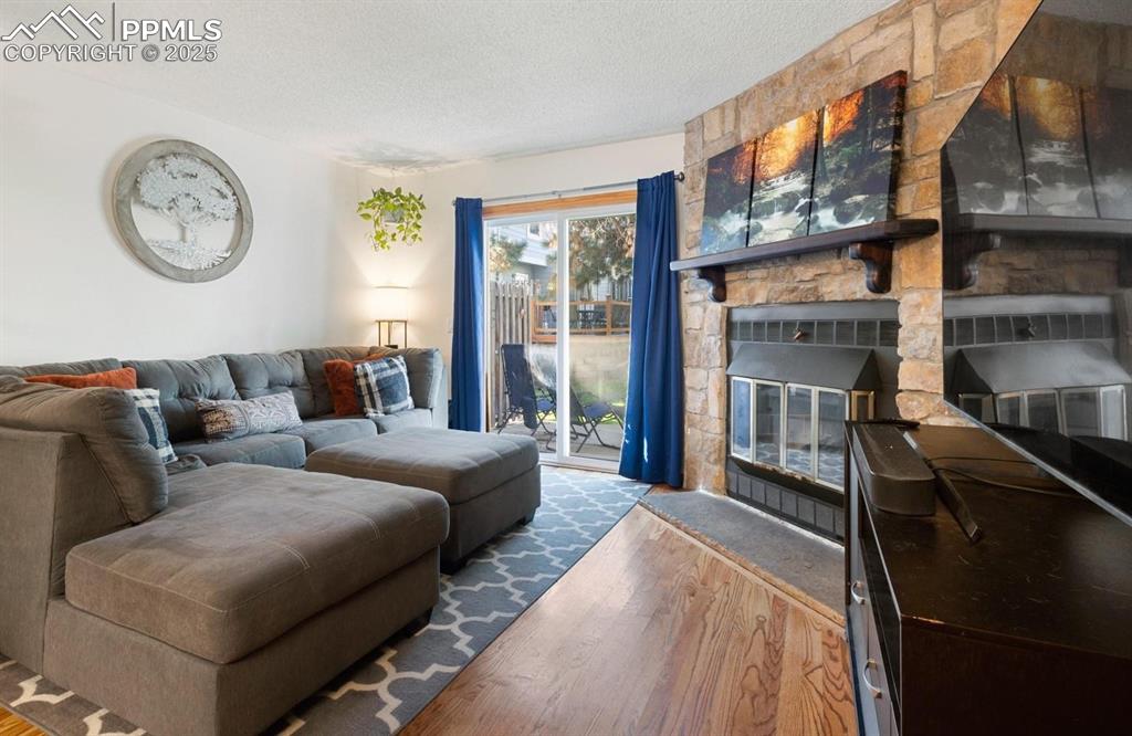 Living area featuring wood finished floors, a textured ceiling, and a stone fireplace