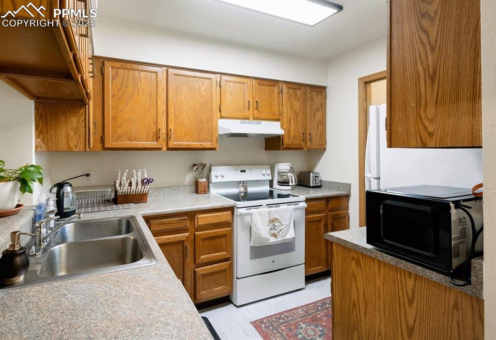 Kitchen with white range with electric stovetop, brown cabinets, black microwave, under cabinet range hood, and light countertops