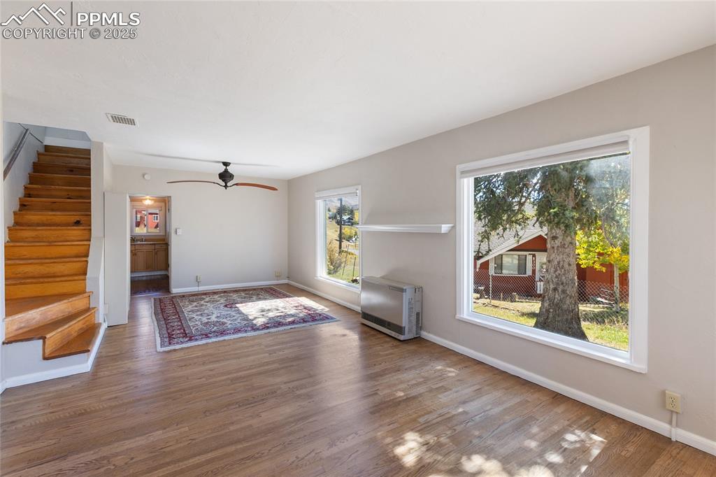 Unfurnished living room with stairway, heating unit, wood finished floors, and ceiling fan